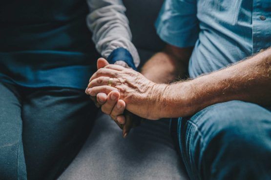 hands of older man and woman holding each other while sitting